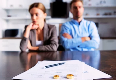 Blurred image of a couple sitting at table with divorce documents with their wedding rings and a pen on. Divorce for Business Owners