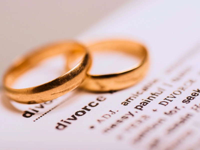 Two gold wedding rings resting on a page of text where the word "divorce" is prominently visible. Divorcing a spouse who hides assets