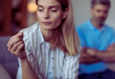 A woman holding her wedding ring while a blurred man is visible in the background, symbolizing themes of divorce, separation, and relationship problems. How to Tell If Your Spouse Is Hiding Assets Before a High-Net-Worth Divorce