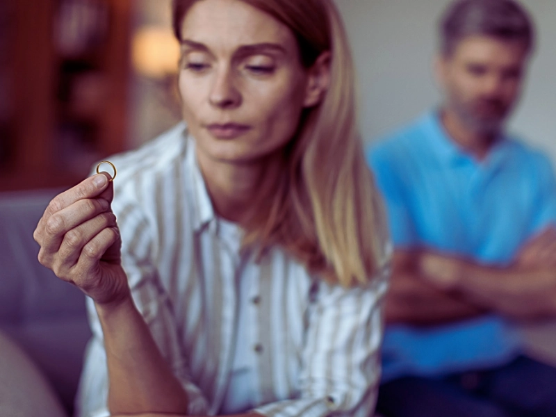 A woman holding her wedding ring while a blurred man is visible in the background, symbolizing themes of divorce, separation, and relationship problems. How to Tell If Your Spouse Is Hiding Assets Before a High-Net-Worth Divorce