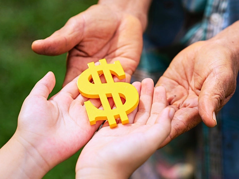 Adult hands placing yellow dollar sign in child's hands How Trusts, Inheritances, and Family Wealth Are Treated in Divorce.