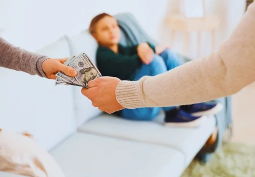 Handing over cash with a child in the background. Parenting Time Reduces Child Support