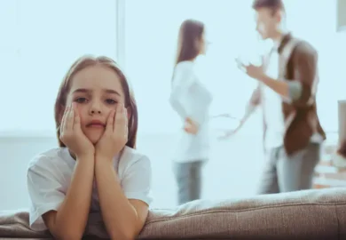 A sad little blond girl dressing a white shirt with his parents fighting behind her Used Against You in an Illinois Child Custody Case