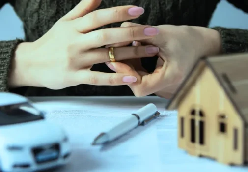 A close-up of a woman's hands removing her wedding ring. In front of her are a house and a car, indicating a separation of assets is imminent. private equity investments in an Illinois divorce