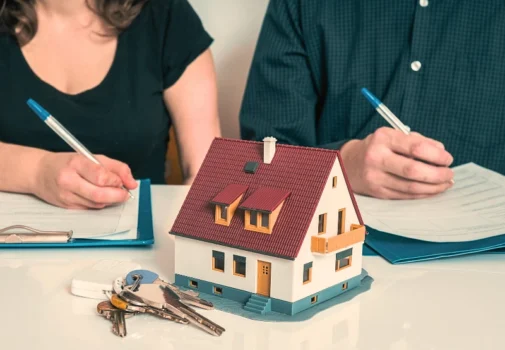 Couple signing real estate papers behind miniature house model and keys. marital property