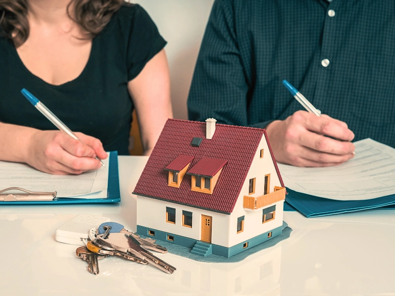 Couple signing real estate papers behind miniature house model and keys. marital property