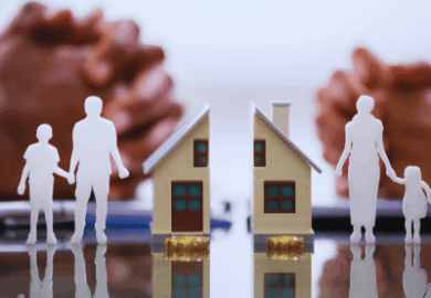 A miniature house split in half, alongside miniature people. In the background, two people with their hands crossed. standard of living after an Illinois divorce, budgeting after divorce
