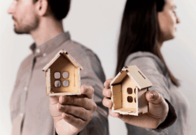 A man and a woman standing back-to-back, each holding half of a house in their hands. the house in an Illinois divorce