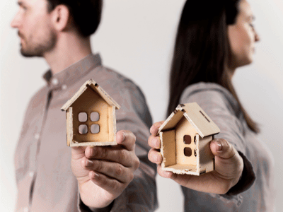 A man and a woman standing back-to-back, each holding half of a house in their hands. the house in an Illinois divorce